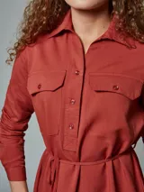 Vestido camisero verde con cuello clásico, mangas largas, cierre frontal con botones, dos bolsillos con solapa en el pecho y cinturón con lazo.