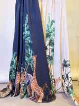 Vestido largo negro con estampado de jungla con palmeras, jirafas y leopardos. Tiene breteles finos, escote en V cruzado y cinturón con apliques brillantes.