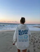 Hoodie blanco con estampado en la espalda que dice "Glassy Waves", "Good Vibes", una flor y las fechas "1971, 1982, 1999".