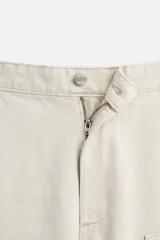 Pantalón color marrón con efecto lavado, corte relaxed fit, cinco bolsillos, aplicación de tira y bolsillo multifunción en perneras, cierre frontal con cremallera y botón.