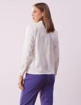 Camisa blanca de gasa, marca Sioni, con cuello con solapa, abertura central con botones y mangas largas con puño y botón.