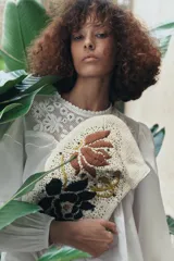 Bolso de mano pequeño confeccionado en hilatura de algodón color beige, con bordado de flores en marrón y negro, aplicación de abalorios y cierre con clip.