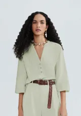 Blusa verde claro a rayas verticales, con cuello en V y cierre frontal con botones. Mangas 3/4 abullonadas y corte holgado.