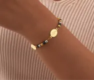 Set de tres pulseras doradas con dijes religiosos: una de cuentas redondas con cruz grande, otra con cuentas negras y dijes de medallas, y otra con cuentas pequeñas y cruz pequeña.