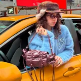 Bolso pequeño tipo clutch o bandolera de cuero color bordó, con efecto arrugado y fruncido en la parte superior y cordones ajustables con herrajes metálicos plateados. Posee una correa larga y fina para llevar al hombro.