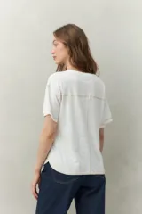 Remera blanca de algodón liviano, de manga corta y cuello redondo. Presenta costuras a contratono visibles en hombros y mangas.