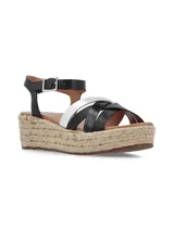 Sandalias de plataforma con suela de yute, tiras cruzadas de cuero negro y plateado, y pulsera al tobillo con hebilla metálica.