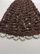Casquete marrón tejido a crochet con detalle de perlas en el borde.
