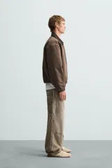 Pantalón gris de corte relaxed fit, con cinco bolsillos, efecto lavado, aplicación de tira y bolsillo multifunción en perneras. Cierre frontal con cremallera y botón.