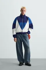 Chaqueta deportiva azul marino, azul y blanca con cuello alto, cierre frontal con cremallera, bolsillos laterales y puños y bajo acanalados.