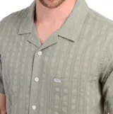 Camisa verde de manga corta con cuello cubano, cierre frontal con botones y bolsillo en el pecho.