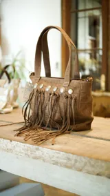 Cartera marrón con textura símil piel de cocodrilo, con flecos y apliques metálicos.