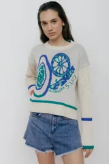 Buzo color crudo con estampado de frutas y texto "La Verduleria S.I.V.I.". Mangas largas con diseño de punto trenzado.