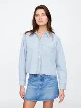 Camisa cropped de jean a rayas verticales celestes y blancas, con cuello clásico, manga larga y bolsillo en el pecho.