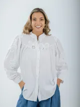 Camisa color crema de broderie, corte holgado, con cuello mao y mangas largas abullonadas con bordados florales.