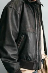 Cazadora bomber de piel color marrón oscuro envejecido, con cuello solapa, cierre frontal de cremallera y puños y bajo en rib elástico. Presenta grabados en relieve en el delantero y la espalda.