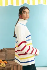 Sweater de punto grueso color crudo, con cuello alto con cierre de cremallera y rayas horizontales en azul, amarillo y rojo.