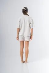 Conjunto de pijama de tela waffle color crema, compuesto por una camisa de manga corta con botones, bolsillo y detalle de broderie, y un short con elástico y cordón en la cintura con terminación de broderie.