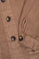 Campera color marrón claro estilo sobrecamisa confeccionada en lino premium. Cuenta con cuello clásico, cierre frontal con botones, un bolsillo de parche en el pecho y dos bolsillos de parche en la parte inferior.