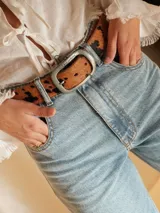 Cinturón de cuero con estampado animal print de vaca, hebilla metálica dorada y reverso de cuero color bordó.