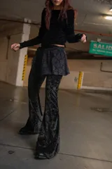 Pantalón acampanado de terciopelo negro con estampado floral y falda corta de encaje superpuesta.