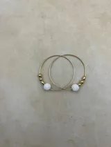 Aros de oro con forma de aro, con una piedra volcánica blanca y pequeñas cuentas doradas.