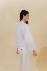 Blusa blanca de lino con cuello mao con volante fruncido y manga larga con puño elástico. En la delantera lleva unas vainillas aplicadas en contratono generando un efecto de dibujo. Se cierra mediante una cartera escondida con botones.