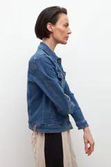 Chaqueta de jean azul medio, de corte clásico, con cuello camisero, bolsillos con solapa en el pecho y cierre frontal con botones metálicos color cobre.