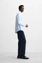 Camisa celeste a rayas verticales blancas, de corte recto, con cuello italiano abierto, manga larga con puños abotonados y cierre frontal con botones.
