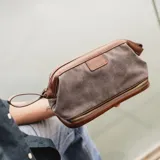 Neceser verde de tela canvas combinado con símil cuero marrón. Tiene apertura superior con cierre metálico estructural, doble bolsillo interno (uno con cierre y otro abierto con división) y base con cierre que actúa como bolsillo extra.