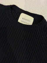 Sweater negro de punto acanalado con cuello redondo y botones decorativos en las mangas.