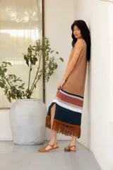 Vestido tejido en hilado de algodón con flecos de gamuza color tostado, con rayas horizontales en el ruedo en tonos negro, blanco, ladrillo y celeste.