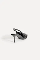 Zapato destalonado de cuero negro con punta fina, tacón fino y detalle de ojales metálicos.