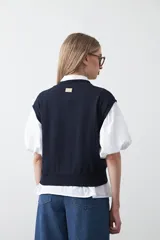 Chaleco de punto color blanco con bordado aplicado de cordón marrón en diseño floral. Presenta cierre frontal de botones al tono, cuello redondo y terminaciones acanaladas en sisas y ruedo.