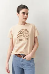 Remera color beige con estampado de una concha marina y texto en color marrón.