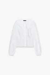 Camisa blanca de popelina de algodón con cuello bobo y mangas largas con elástico en los puños. Detalle de puntilla a tono en cuello y ruedo. Cierre frontal con botones.