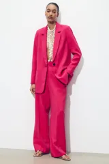 Blazer fucsia de cuello solapa y manga larga con hombreras. Detalle de tejido efecto arrugado. Bolsillos delanteros de vivo. Cierre frontal con un botón.