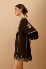 Vestido corto negro con bordado de hilo blanco, escote en V y mangas largas abullonadas.