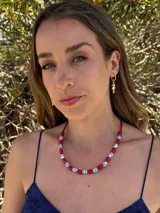Collar corto con cuentas de cerámica rojas y blancas con estampado de flores azules, engarzadas en hilo rojo. Cierre con cadena de acero quirúrgico plateado.