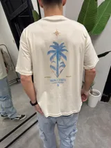 Remera color crema de algodón con estampado de palmera azul y brújula en la espalda.