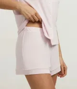 Conjunto de pijama americano compuesto por una blusa de manga corta con cuello solapa y abotonado frontal, y un short con cintura elástica y lazo. El conjunto es liso en color rosa pálido, con vivos contrastantes en el borde de las prendas.