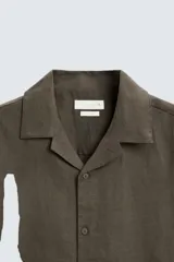 Camisa color marrón oscuro de corte relaxed fit, confeccionada en tejido de lino. Tiene cuello bowling, manga corta, bajo con aberturas laterales y cierre frontal de botonadura.