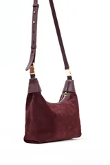 Bandolera tipo hobo de gamuza color ciruela, con correa ajustable de cuero marrón oscuro y herrajes dorados. Presenta un cierre superior con cremallera.