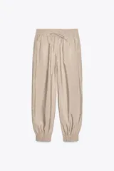 Pantalón de tiro medio color beige, con cintura elástica ajustable con cordones, bolsillos delanteros y puños elásticos en los tobillos.