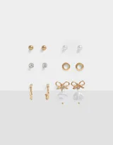Set de seis pares de aros dorados con distintos diseños: aros tipo botón con perla, aros tipo botón con strass, aros tipo botón dorados, aros de argolla y aros colgantes con dije de perla y moño.