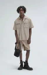 Camisa beige de manga corta, estilo técnica, confeccionada en microfibra liviana. Con doble bolsillo frontal y broches en lugar de botones.