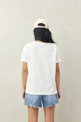 Remera blanca de manga corta confeccionada en algodón liviano con textura levemente jaspeada. Presenta tajos laterales y costura central al frente.