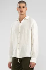 Camisa de manga larga color blanco hueso, confeccionada en lino, con cuello clásico y cierre frontal con botones de coco.