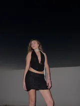 Conjunto de top halter y minifalda, ambos de lentejuelas negras. El top es corto y tiene un escote pronunciado. La falda es ajustada y de tiro alto.