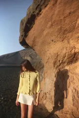 Chaqueta de punto amarilla con cuello redondo, manga larga y cierre frontal con botones. Detalle de volantes en los bordes.